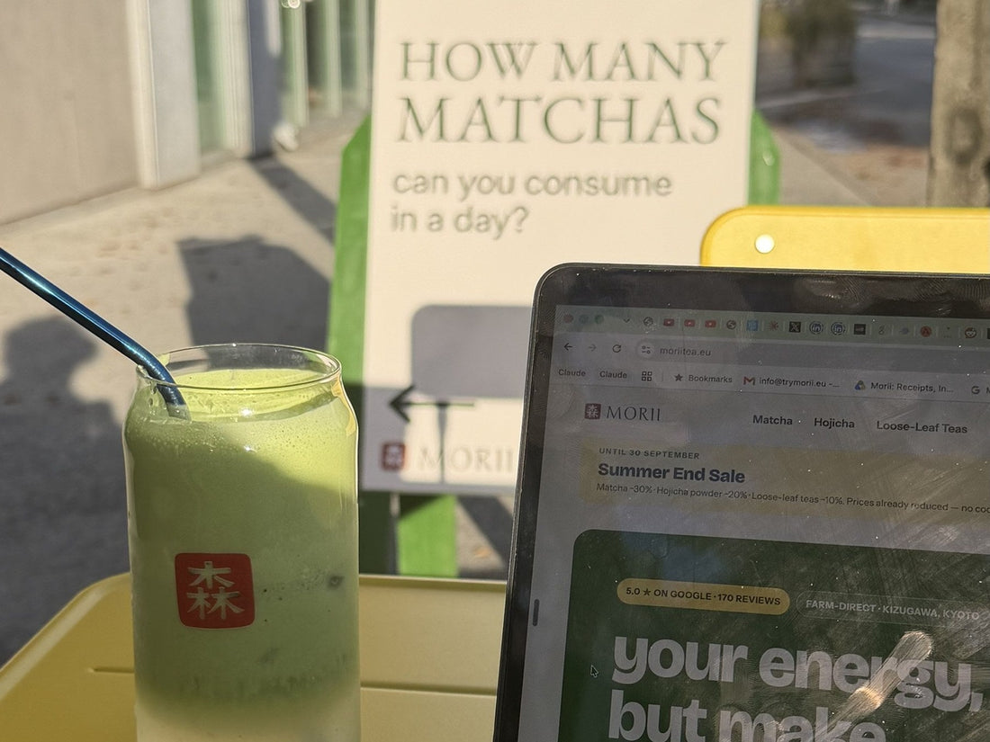 A sign outside Morii Teahouse in Tallinn asking how many matchas you can consume in a day, next to an iced matcha latte and a laptop